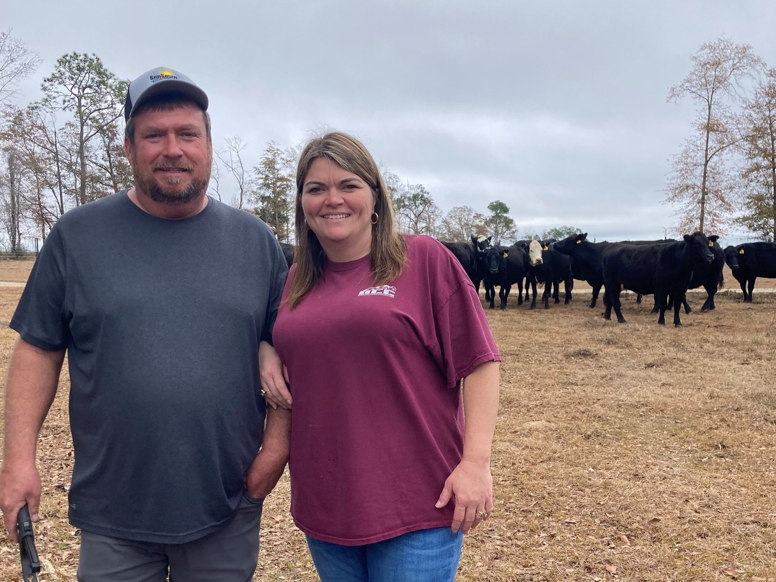 Farmers standing together in a field with black cows in the background, showcasing rural agriculture and livestock management.