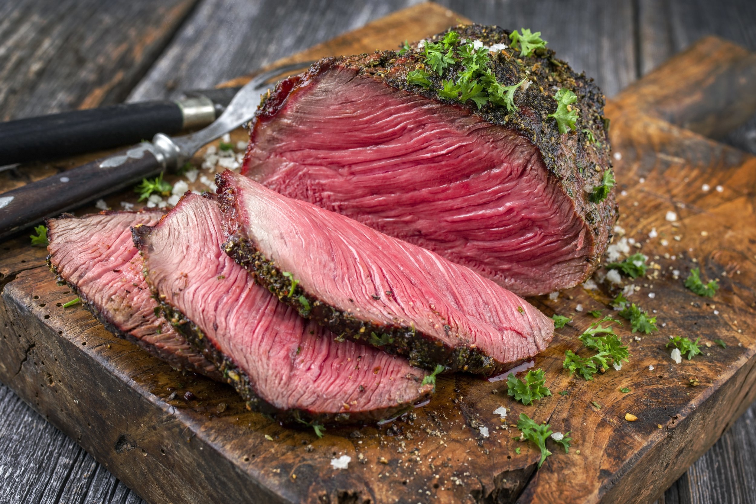 Barbecue wagyu point steak sliced as close-up on a cutting board Sliced roast beef on a wooden cutting board, garnished with fresh herbs and coarse salt, showcasing a juicy pink interior and a seasoned crust. Perfect for showcasing delicious meat recipes or cooking techniques.